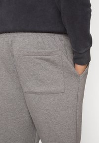 Szare spodnie dresowe wykonane z miękkiej mieszanki bawełny, z elastycznym pasem, bocznymi kieszeniami oraz jedną tylną kieszenią. Gładka faktura, luźny krój.