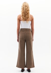 Ruske leve široke hlače iz denima z visokim pasom, dvema zadnjima žepoma in nerobljenim robom. Nošene z belo majico brez rokavov.