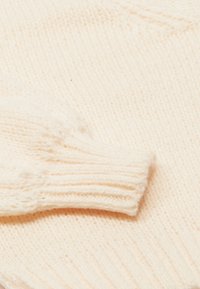 Krém színű kötött pulóver bordázott mandzsettákkal és puha, texturált anyagból készült. A dizájn egyszerű, látható minták vagy díszítések nélkül.