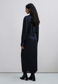 Vestido largo azul marino con rayas verticales, puños abotonados y cintura ajustada. El material parece suave; se lleva con botas negras de tobillo.
