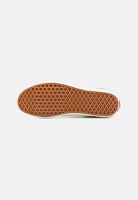 Suola di sneaker, in gomma marrone con un motivo esagonale testurizzato, lati bianchi e un piccolo accento rosso sul tallone, vista dal basso.