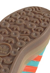 Sole tenisky Adidas s texturovanou hnědou gumovou spodní částí, kruhové vzory a logo. Vrchní část je v barevných odstínech mátové zelené a oranžové.