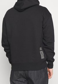 Schwarzer Hoodie mit lockerer Passform, ausgestattet mit einer Kapuze, gerippten Bündchen und seitlichen Akzenten aus einem kontrastierenden Material. Weicher Stoff.