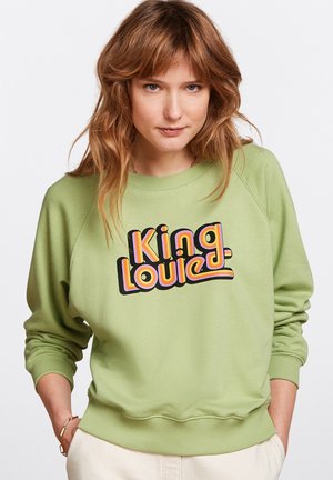 Felpa verde con scollatura tonda e maniche lunghe, caratterizzata da una grande grafica in stile retro che dice "King Louie" in colori vivaci.