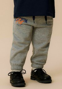 Grijze sweatpants met elastische boorden, voorzien van een blauwe en oranje "Stadium Play" print. Gecombineerd met zwarte veterschoenen. Zachte stof textuur.