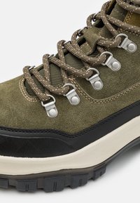 Zielone zamszowe buty trekkingowe z czarnymi gumowymi akcentami, metalowymi oczkami i fakturowanymi sznurówkami. Posiadają amortyzowaną podeszwę dla lepszej przyczepności.