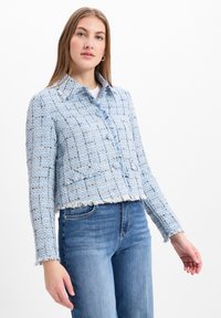 Lichtblauwe tweedjasje met een cropped ontwerp, rafelige randen en een kraaglijn; voorzien van knoopsluiting en een subtiel ruitpatroon.