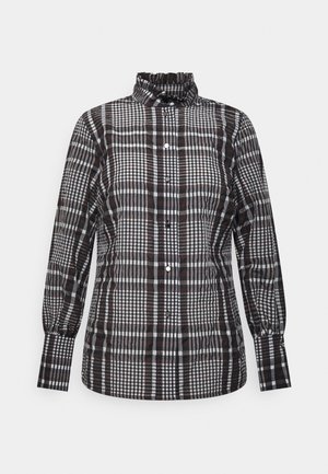 Chemise à manches longues à carreaux noirs, blancs et marron avec col haut volanté et fermeture boutonnée sur fond uni.