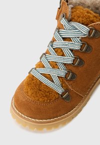 Bocanci din suede maro cu sireturi albastre și albe în dungi, căptușeală moale din fleece, ochiuri din metal și o talpă rugged, bej, cu un tread texturat.