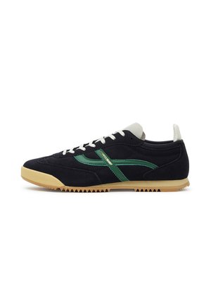 Czarny niski sneaker z beżową podeszwą, białymi sznurówkami i zielonym paskiem bocznym z napisem „POMPEII BRAND” na białym tle.