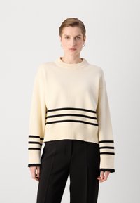 Crème gebreide trui met zwarte horizontale strepen aan de zoom en mouwen, met een ronde halslijn en een relaxed fit.