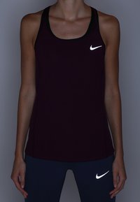 Personne portant un haut Nike sans manches noir et des leggings foncés, tous deux portant des logos Nike blancs réfléchissants sur la poitrine et la cuisse.