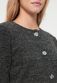 Μαύρο και άσπρο υφασμάτινο μπλουζάκι με υφή, που διαθέτει στρογγυλή λαιμόκοψη και τρία διακοσμητικά ασημένια κουμπιά με όψη κρυστάλλου.