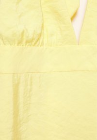 Gros plan d'un tissu jaune doux avec une couture froncée et un détail d'encolure en V.