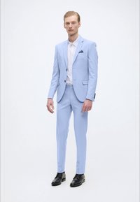 Hellblaues Anzug aus Stoff mit glatter Textur, bestehend aus einem Ein-Knopf-Blazer, passenden Hosen und einem Taschentuch. Schwarze Schuhe.