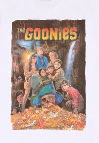 Bílé tričko se barevným grafickým motivem postav z "Goonies", obklopených pokladem a lebkou, na pozadí jeskyně.