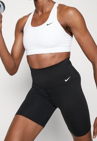 Biały stanik sportowy z cienkimi ramiączkami i czarnym logo Nike, w połączeniu z czarnymi szortami sportowymi o wysokim stanie z małym białym logo Nike.