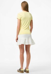 Geel T-shirt met korte mouwen gecombineerd met een witte gerimpelde rok. De outfit wordt compleet gemaakt met bruine en gele sneakers.