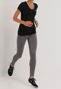 Femme en train de courir, portant un t-shirt noir Nike, un legging gris, des baskets noires Nike et une montre de fitness blanche au poignet gauche.