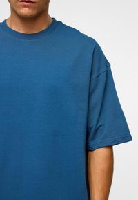 Blauwe katoenen t-shirt met korte mouwen, ronde halslijn, losse pasvorm, gladde textuur en minimale stikseldetails.