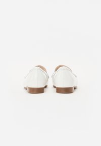 White leather shoes with a rounded toe, low heel, and minimal stitching. Smooth texture with a slight shine and a natural wood-colored sole.