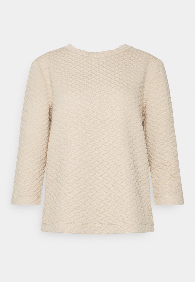 Haut en maille texturée crème à manches longues avec un motif chevron subtil et un col rond, présenté sur un fond uni.
