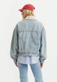 Lichtblauwe denimjack met een schapenvachtkraag, boxy pasvorm, verlaagde schouders en knoopdetails, gecombineerd met een lichtblauw shirt en jeans.