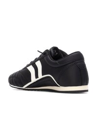 Zapato deportivo negro con parte superior de cuero texturizado, rayas blancas, tacón redondeado y suela en contraste. Presenta un diseño de cordones y un collar acolchado.