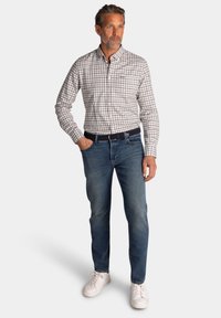 Mannen geruit shirt in lichtgrijs en marineblauw, gecombineerd met blauwe denim jeans. De schoenen bestaan uit witte sneakers, met een donkere riem als accent.
