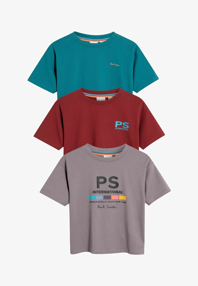 Drie t-shirts met korte mouwen: teal met gouden tekst, bordeauxrood met een blauw grafisch ontwerp, en grijs met zwarte print, allemaal gemaakt van zacht katoen.