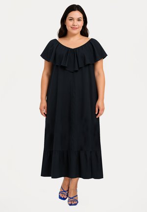 Sorte off-shoulder maxikjole med lagdelt flæse-halsudskæring og en flagrende nederdel, parret med blå stroppesandaler. Glat stoftekstur.