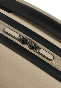 Beige koffer met een gestructureerd oppervlak, zwarte ritsaccenten en een metalen ritslus met de opdruk "REDOLZ."