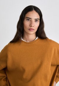 Suéter oversize color mostaza con cuello redondo y mangas largas, hecho de una tela suave con un acabado texturizado.