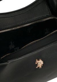 Czarna skórzana torebka z złotym zamkiem błyskawicznym i złotym tłoczonym logo na zewnątrz. Wnętrze wyłożone ciemnym materiałem z subtelnym wzorem.