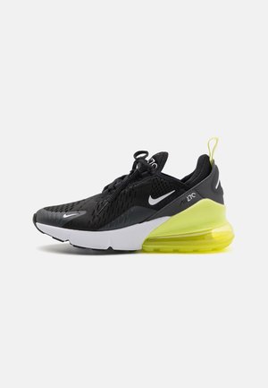 Czarno-szary sportowy sneaker z białą podeszwą, żółtym poduszkowym obcasem, białymi znakami Nike, siateczkową cholewką i pętelką z tyłu.