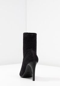 Botín negro con acabado de tejido texturizado, tacón alto estilo stiletto y un ajuste ceñido alrededor del tobillo. Diseño sencillo sin adornos.