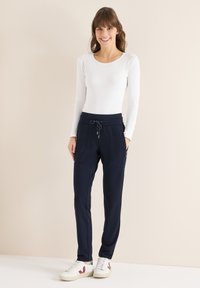 Marineblauwe joggerbroek met een trekkoord in de taille, twee zijzakken en omgeslagen enkels, gecombineerd met een aansluitend wit shirt met lange mouwen.