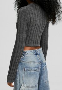 Woman wearing a gray ribbed long-sleeve cropped sweater and high-waisted light blue wide-leg jeans with large back pockets.