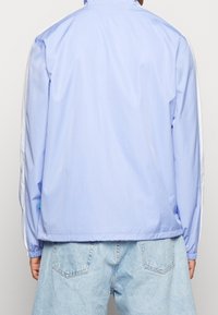 Chaqueta azul claro con líneas verticales, detalles blancos en las mangas y puños elásticos. Fabricada con un tejido suave y ligero.