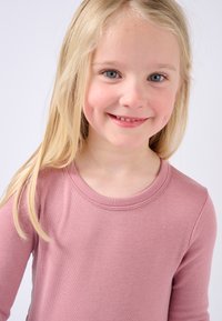 Camicia a maniche lunghe di colore rosa chiaro con scollatura rotonda e texture liscia, indossata da un bambino con capelli biondi lisci e occhi azzurri.