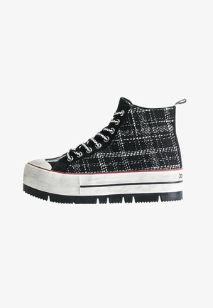 Zwart-wit geruite high-top sneaker met een dikke witte rubberen neuskap, zilveren ogen en een dikke zwarte zool met rode accenten.