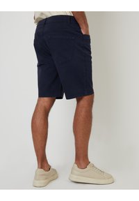 Pantalones cortos azul marino de mezcla de algodón, con dos bolsillos traseros y un corte recto, combinados con zapatillas ligeras color beige.