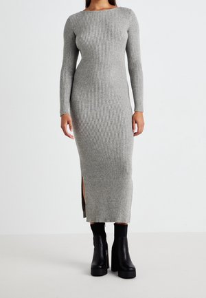 Mujer con un vestido largo gris de punto acanalado, de manga larga y con aberturas laterales, combinado con botines negros con plataforma.