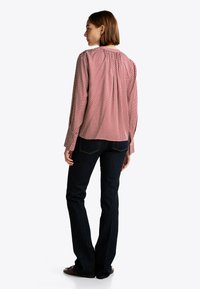 Rød og hvid mønstret skjorte med lange ærmer og indsamlet rygdetalje, parret med mørkeblå flagrende jeans og brune sko.