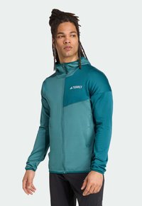 Hooded zip-up jacket in teal with a textured finish. Features a contrasting chest panel and logo. Long sleeves and fitted design.