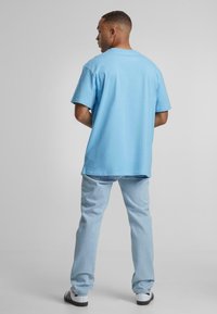 Camiseta de algodón azul claro con un corte relajado, cuello redondo y mangas cortas, combinada con jeans de mezclilla azul claro y zapatos en blanco y negro.