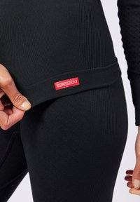 Schwarze thermische Leggings mit einem strukturierten Muster und einem sichtbaren roten Etikett, die ein anliegendes Design und einen elastischen Bund zeigen.