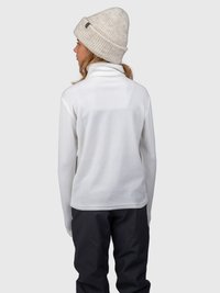Donna che indossa una giacca in pile bianca, pantaloni neri e un berretto lavorato a maglia beige, di spalle su uno sfondo grigio neutro.