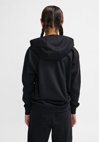 Schwarzer Kapuzenpullover mit lockerer Passform, strukturiertem Stoff und gerippten Bündchen. Die Rückseite verfügt über eine große Kapuze und keine sichtbaren Logos oder Muster.
