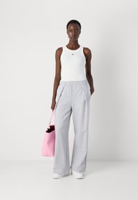 Hvit tanktopp med en liten grønn logo, grå vide joggebukser og en rosa totebag. Modell iført hvite sneakers. En enkel og uformell antrekk.